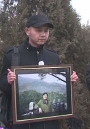 图为曹东2012年出狱后为妻子下葬时怀抱妻子遗像。