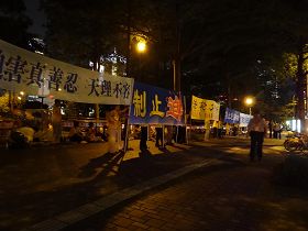 '法轮功学员八日傍晚在君悦饭店对面打开各种抗议横幅，以静坐、炼功方式表达诉求。'
