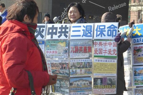 '退党义工通过各种方式让大陆游客了解真相，包括手举真相展板、播放真相广播、发小册子、挂横幅等等，图为义工王女士在向游客展示真相展板。'