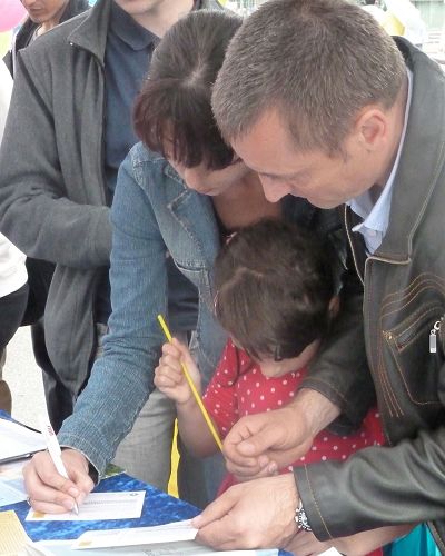 图2：一家人都来帮忙营救在中国深陷牢狱的法轮功学员，先是母亲（左）签名，然后是父亲。