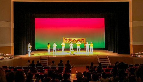 图1：法轮功学员在饭岛町文化节舞台上演示法轮功<span class='voca' kid='86'>功法</span>，并有学员在一旁解说。