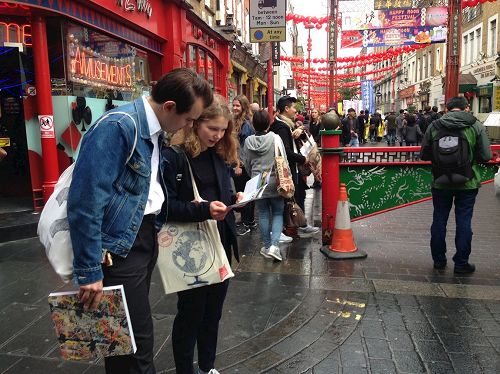 '图6：二零一六年十月一日下午，在伦敦唐人街，法轮功学员的反迫害游行队伍经过后，一对年轻人在非常专注地阅读真相传单'