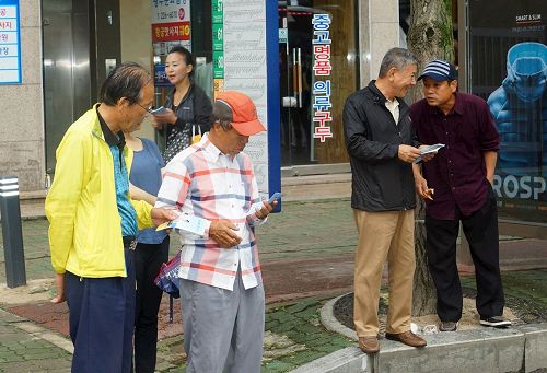 '图4：二旁的民众接过法轮功学员分发的真相资料后，马上阅读。'