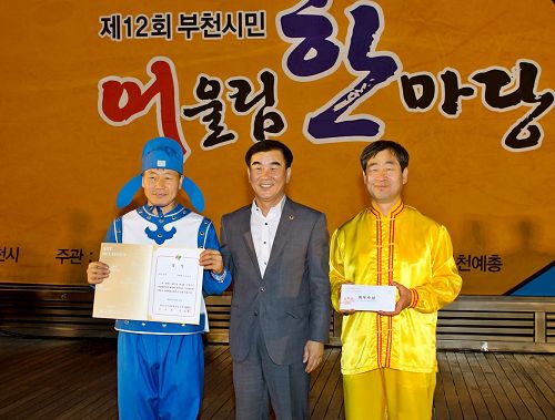 '图6：韩国京畿道议会文化观光委员长（中）给参加本次庆典活动获一等奖——最优秀奖的法轮功团体颁奖。'