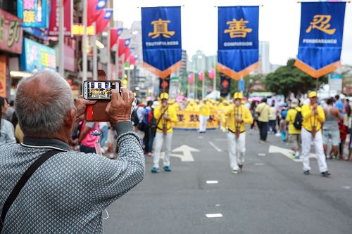 '图4：淡水环境艺术节游行，“真、善、忍”队伍最受瞩目，不少民众拿出手机拍照留影。'