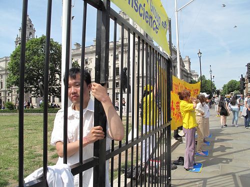'图5：二零一七年七月十八日，杨博士在英国议会大厦前扮演模拟牢笼中的学员'