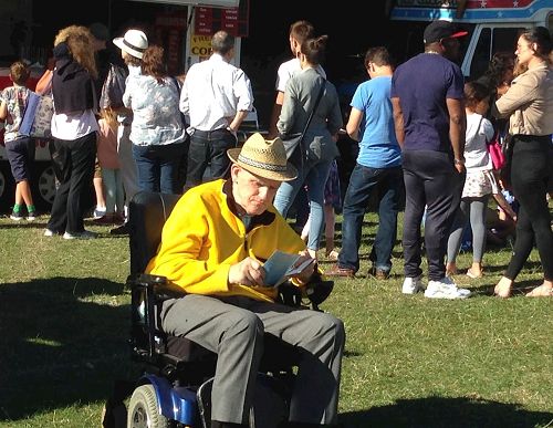 '图9：二零一七年六月二十五日，在东芬诗丽节上，坐在轮椅上的老人麦克（Mike）认真阅读真相传单并签名反迫害。'