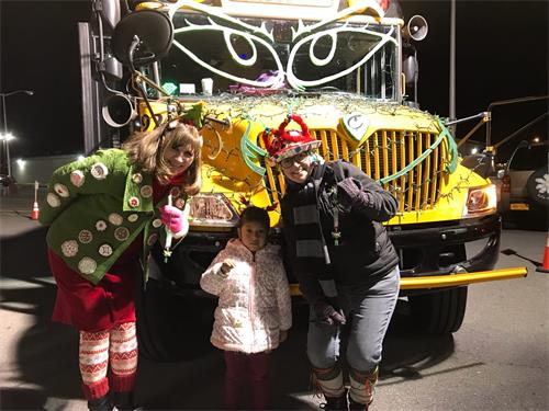 两位校车花车上的老师身着节日服装，手拿着法轮功学员赠与的中英文“法轮大法好”的小莲花和孩子们愉快地合影。