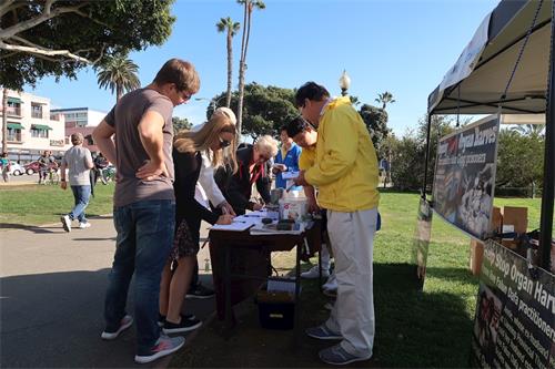 '图8：圣莫妮卡海滩公园的游客签署停止活摘器官的请愿书。'