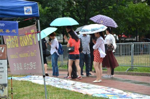 '图7：集会期间下起了大雨，但中国大陆游客仍冒雨观看揭露中共迫害法轮功的真相展板。'