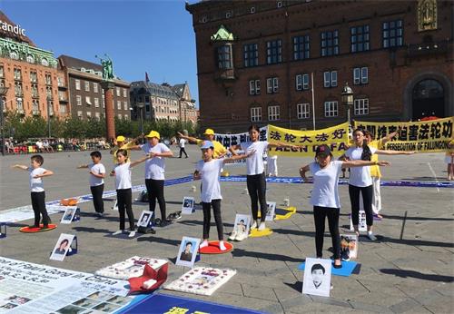 '图2：夏令营的孩子们周六下午参加哥本哈根市政厅广场的七·二零反迫害活动，展示法轮功五套<span class='voca' kid='86'>功法</span>'