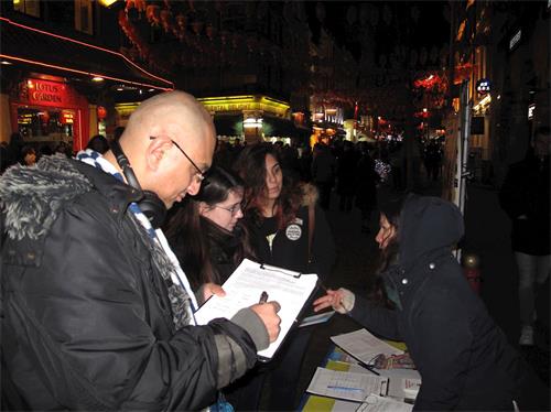 '图4：二零一九年二月十日，在伦敦唐人街，一位在伦敦工作的孟加拉裔男士（左）和两位从巴西来伦敦旅游的女青年驻足倾听真相，接着签名支持法轮功学员反迫害'