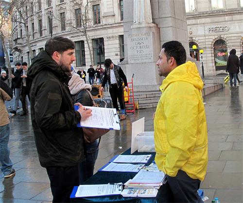 图5：二零一九年二月十日，最近曾去中国大陆旅游的英国年轻人约翰（左）在圣马丁广场与一位法轮功学员深入交谈，他签名反迫害并表示要学法轮功