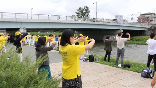'图1～2：当天早晨九点到十一点，法轮功学员在京都市政府附近的御池大桥（Oike-ohashi Bridge）下鸭川河畔的集体炼功，吸引了许多有缘人驻足了解法轮功。'