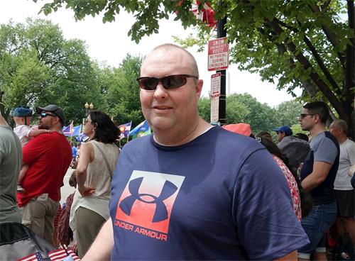 '图10：来自弗吉尼亚州的约翰第一次来现场观看国庆日游行，他用手机拍摄下法轮功团体的游行场面。'
