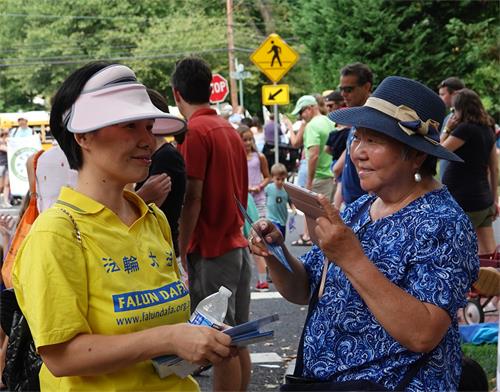 9：华裔居民张艳卿女士用手机拍摄法轮功学员的游行场面，并向法轮功学员了解真相。
