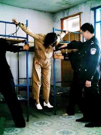 酷刑演示：人被挂在两个单人床中间，两手戴着手铐，挂在单人床上边的铁栏杆上，在把床向两边拉开，吊起来