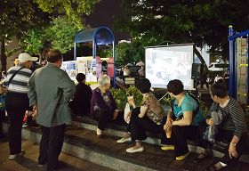 大陆游客逛高雄六合夜市，累了歇一会儿，刚好来看看展板、电视，了解法轮功真相。