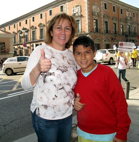 图3：二零一四年十月四日，法轮功学员在马德里举行游行，一位小男孩和妈妈一起认真观看并用iPad拍摄游行队伍，伸出大拇指赞叹法轮功