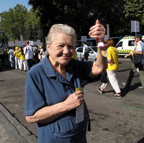 图4：法轮功学员在马德里举行大游行，一位西人老太太站在路旁从头到尾观看游行队伍，照相时，她高兴地举起前面经过的法轮功学员送给她的手工莲花