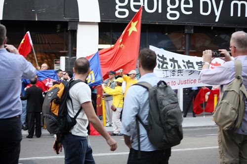 在悉尼主街乔治街上，亲共暴徒抢夺法轮功横幅。路过的澳洲民众纷纷拍照，并谴责暴徒的行径。