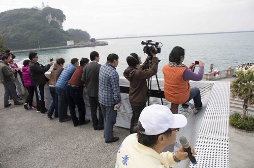 几位大陆游客快快登上雄镇北门高处看台，拿起手机、相机拍下法轮功学员给师父拜年的合照。