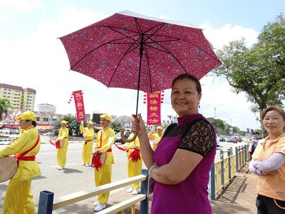 邓女士开心的撑着雨伞站在路旁观看游行。