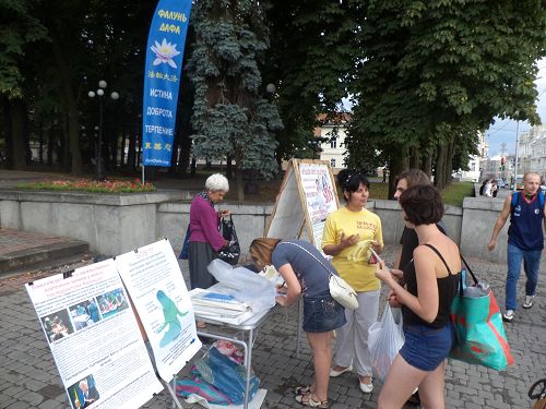 图7：在哈尔科夫市的真相点，人们经过时看到揭露中共酷刑折磨法轮功学员的图片，纷纷驻足了解真相。明白真相后，人们立即在“反对中共强摘法轮功学员器官”的征签表上签名。
