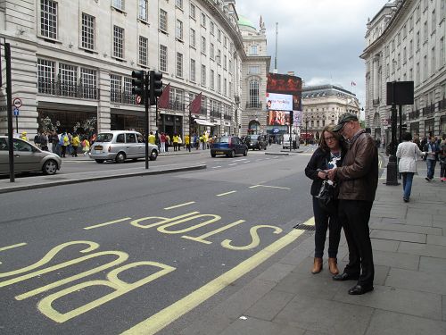 图8：从诺丁汉郡来伦敦探亲的汤姆普森和芭芭拉夫妇在皮卡迪利大街上看到法轮功游行队伍，接过真相传单认真阅读起来