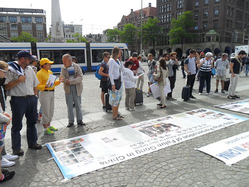 图2-7：荷兰学员在首都阿姆斯特丹达姆广场向各国游客传播真相，他们有的认真阅读真相展板，有的签名支持制止迫害，起诉迫害元凶江泽民。