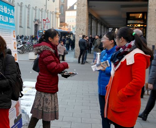 '图6：慕尼黑的法轮功信息展位上，一位法轮功学员（左）正在向两位华人讲述法轮功真相。'