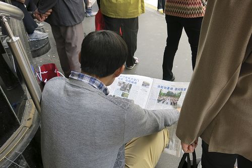 图2：一名大陆游客坐在商场门前的台阶上认真地阅读真相资料，了解法轮功真相。