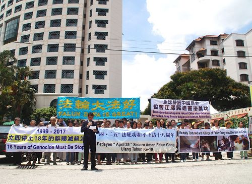 '图1:纪念四二五和平上访十八周年,部份马来西亚法轮功学员顶着烈日,在中共驻马大使馆附近举行集会。法轮功学员代表关先生宣读中文文告。'