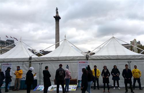 图1-2：二零一八年十月二十七日，法轮功学员在伦敦特拉法加（Trafalgar Square）广场北平台发放真相传单、炼功、讲真相、征签反迫害