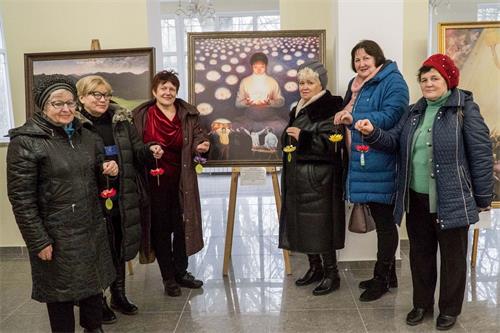 '图1：观看画展的俄罗斯民众手持纸莲花和法轮功学员创作的画合影'