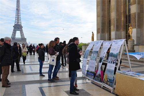 '图1～2：二零一八年十一月四日，法轮功学员冒着寒风在巴黎艾菲尔铁塔的人权广场上传播法轮功的真相。许多游人驻足了解真相。'