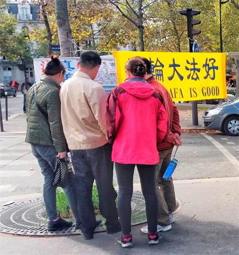 '图：大陆游客在巴黎艾菲尔铁塔真相点观看揭露中共迫害法轮功的展板。'