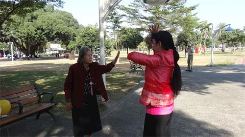 '图8：现年八十几岁的蔡老太太（左），巧遇法轮功集体活动，她走近了炼功队伍，展开双臂跟着学炼，旁边学员热心的教她炼功。'