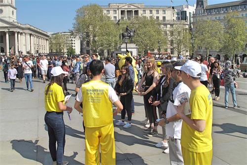 '图8：一群来伦敦旅游的法国年轻人在法轮功学员纪念“四·二五”和平上访二十周年现场尝试学炼法轮功第二套功法动作。学员问他们第一次尝试炼功的感受时，她们回答：感到“美好”、“平和”、“愉悦”。'