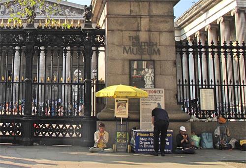 '图15：二零一九年四月二十一日，大英博物馆门前，两位法轮功学员在打坐，一位西人默默走过来签名。'