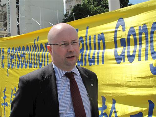 '图10：二零一九年七月十六日，英国会议员帕特里克·格雷迪（Patrick Grady MP）来到法轮功学员“反迫害二十周年”集会现场表支持，他站在“请伸出援手制止迫害法轮功（Please help to stop the persecution of Falun Gong）”横幅前接受采访'