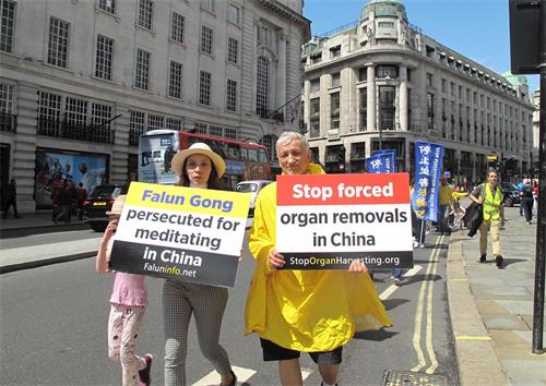'图6：英国法轮功学员泽克（Zek，右）走在伦敦“反迫害二十周年”游行队伍中，他从一九九八年开始修炼法轮功，二十年来一直在呼吁英国民众和国际社会关注中共迫害法轮功反人类罪行。'