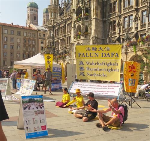'图1：二零一九年八月二十四日，法轮功学员在德国慕尼黑玛琳广场举办活动。图为民众跟法轮功学员学炼功法。'