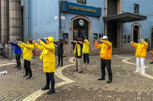 '图1：法轮功学员在音乐厅旁举办讲真相活动。学员们在雨中展示功法。'