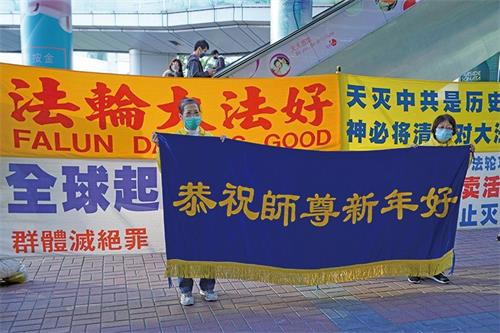 '图1:无惧打压,法轮功学员坚持讲真相,希望更多世人选择良知。在红磡真相点讲真相的法轮功学员恭祝李洪志先生新年快乐。'
