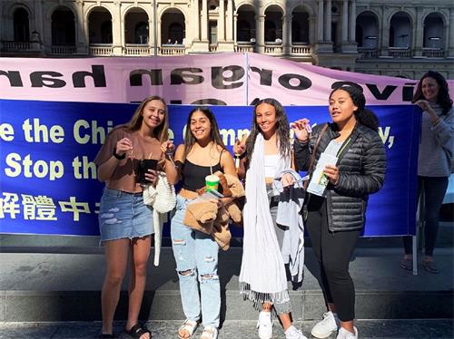 '图13：四位澳洲女孩在了解法轮功真相后纷纷签字呼吁停止迫害。她们手握法轮功学员送给她们的莲花小吊坠，在制止迫害的真相横幅前集体拍照。'