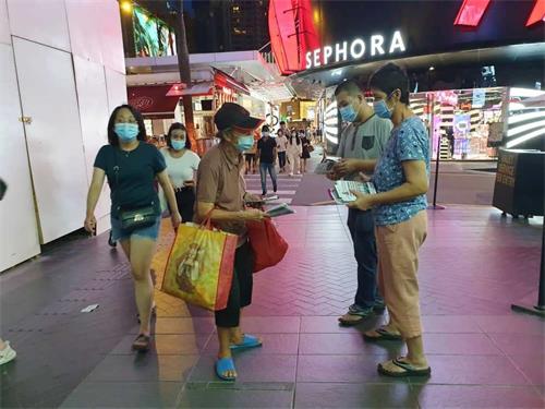 '图4:国雄与母亲慧锦正在给过往路人发法轮功真相资料。'