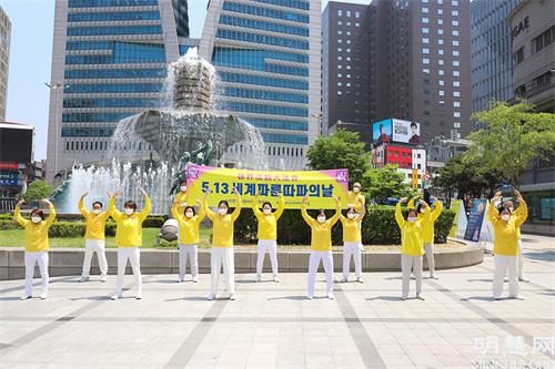 图2：5月13日，部分首尔西部和中部的法轮功学员们在首尔市中心新世界百货店附近的大型喷泉前举行了集体炼功、派发传单等洪法活动。图为他们在集体炼功的场面。