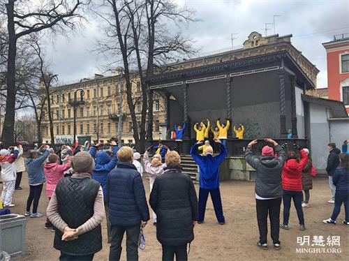 '图1：二零二一年四月二十四日，俄罗斯圣彼得堡市法轮功学员在庆祝“世界太极拳和气功日”活动中介绍和演示法轮功，台下的观众跟着学炼功法动作。'