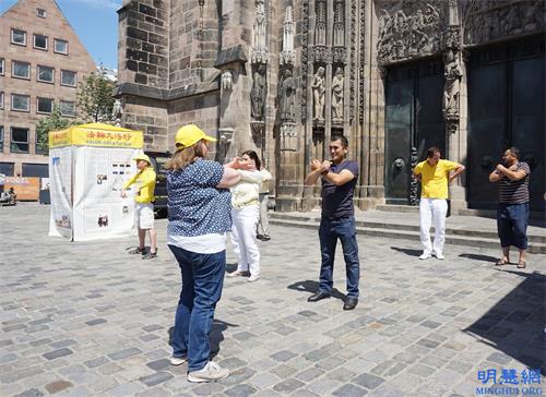 '图2：二零二一年六月三日，法轮功学员在德国纽伦堡市的洛伦兹教堂前举行信息日，两位乌兹别克斯坦游客当场学习法轮功功法。'